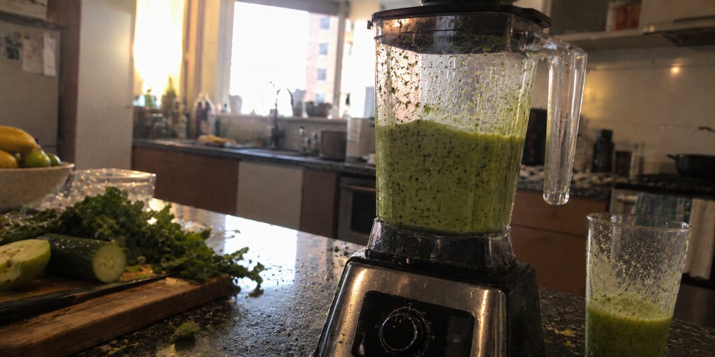 Liquidificador com a vitamina verde batida, na cozinha, com o copo ao lado